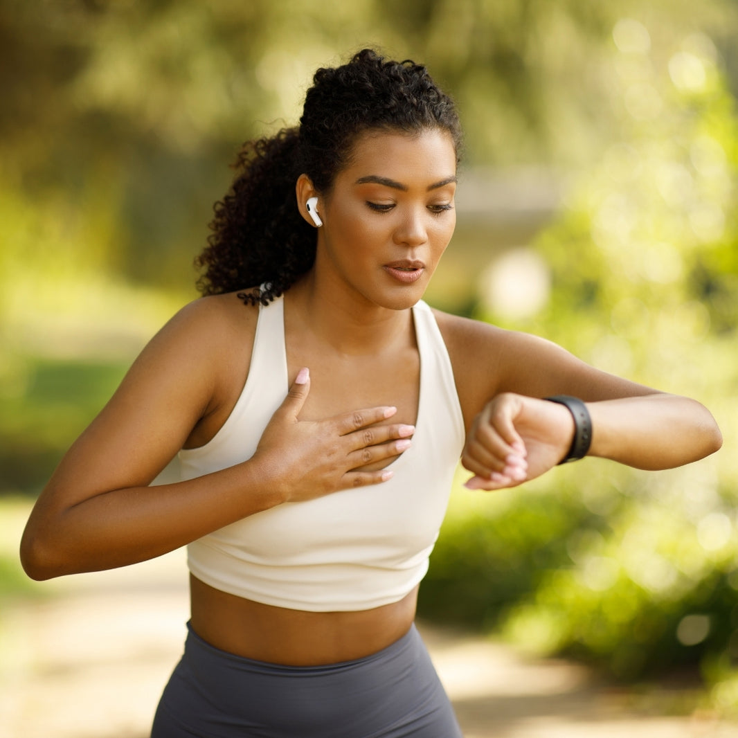 A woman in athletic wear, featuring a cream sports bra and gray leggings, checks her fitness watch in an outdoor park setting.